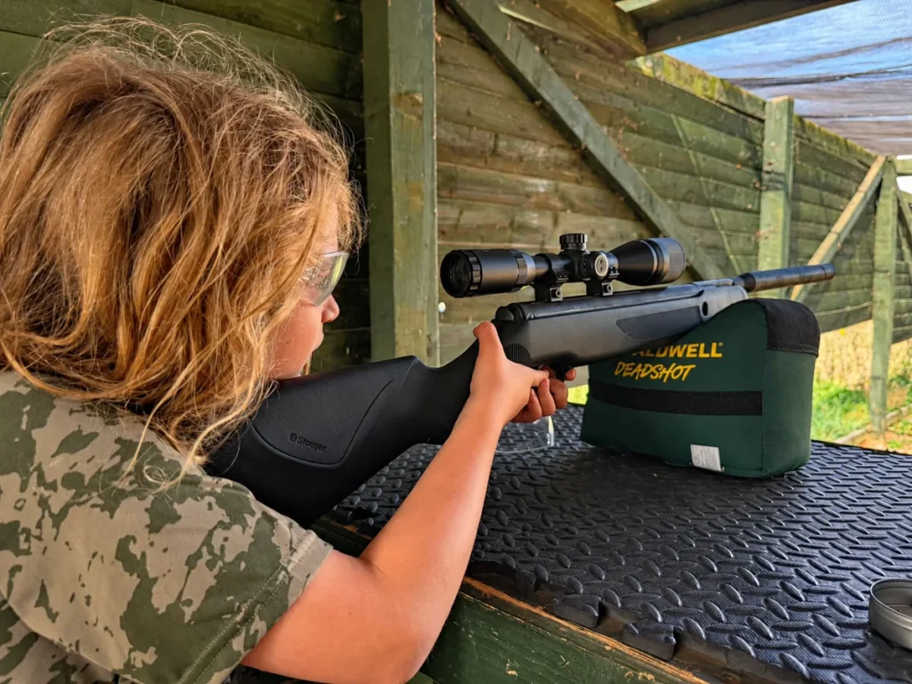 A participant wearing safety glasses aiming a supported air rifle at Escot Park, Devon.