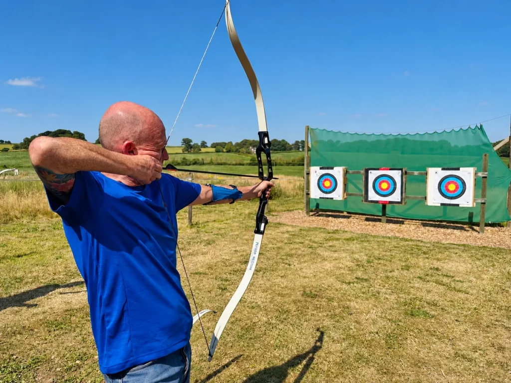 A participant aiming a recurve bow at outdoor archery targets at Escot Park, Devon.