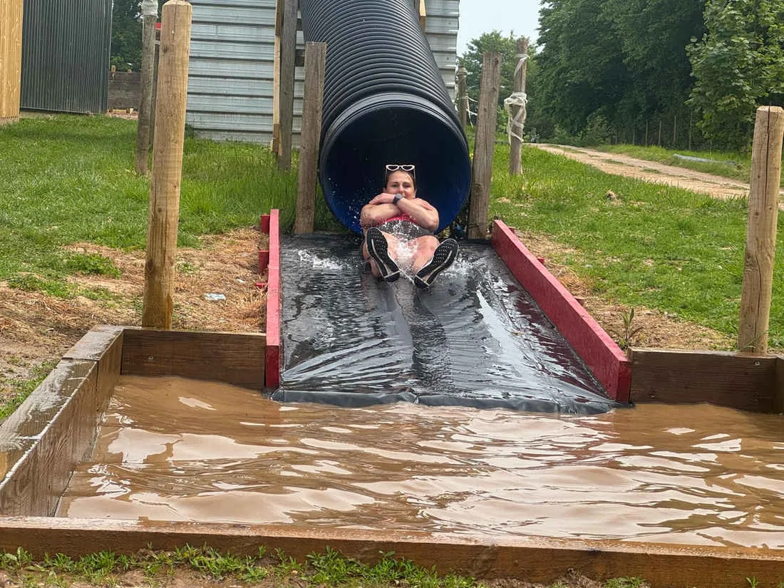 A participant sliding from a tube into the water obstacle on the assault course near Exeter.
