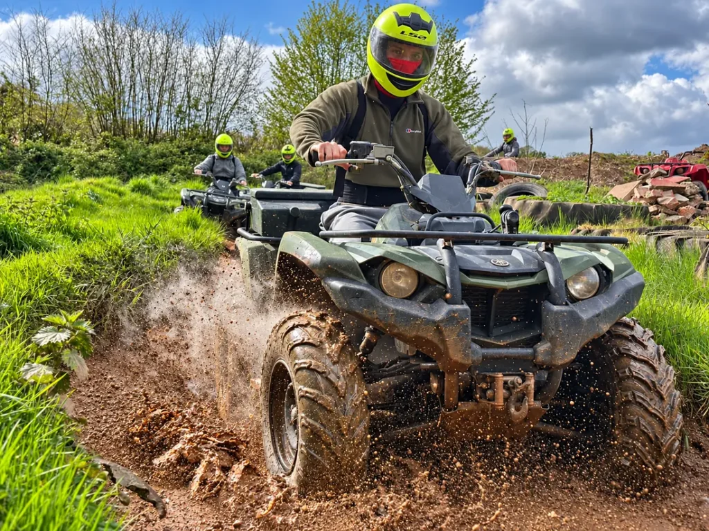 A helmeted rider driving a quad bike through mud at Escot Park, Devon, with other riders behind.